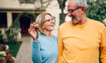 coppia di anziani con le chiavi in mano e in piedi davanti a casa